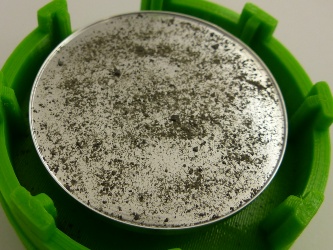 Odrazivý hliníkový povrch s kontaminací simulantem měsíčního regolitu.